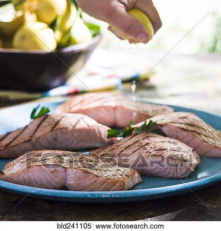 Stock Photography - Hand squeezing juice from lemon onto plate of salmon. Fotosearch
