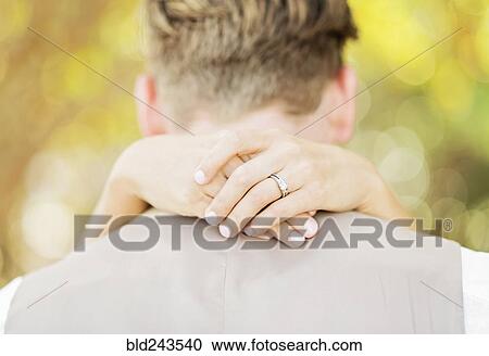 Stock Image - Hands of Caucasian bride hugging groom outdoors. Fotosearch