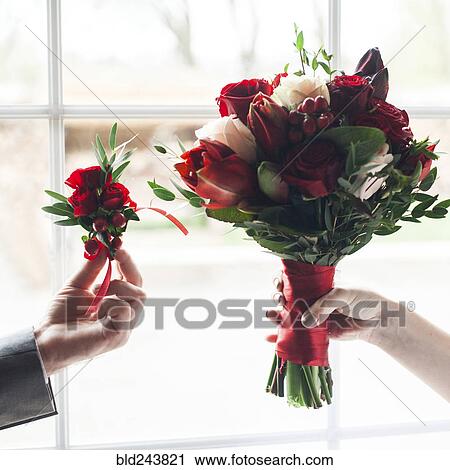 Stock Image - Hands of Caucasian couple holding corsage and bouquet of flowers. Fotosearch