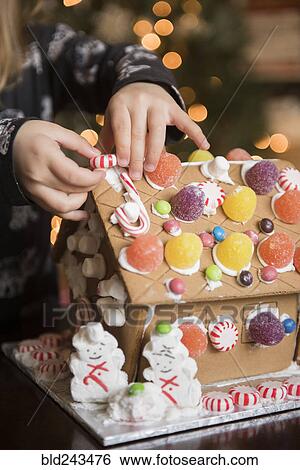Stock Photograph - Hands of Caucasian girl decorating gingerbread house with candy. Fotosearch
