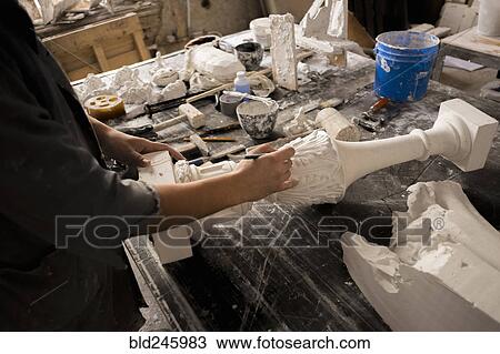 Stock Image - Hands of Caucasian sculptor carving plaster piece. Fotosearch
