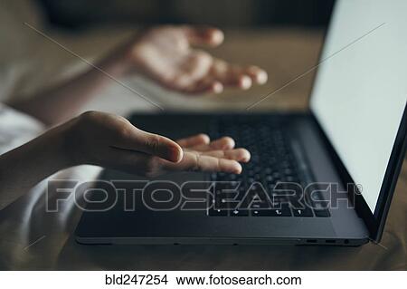 Picture - Hands of Caucasian woman gesturing at laptop in bed. Fotosearch
