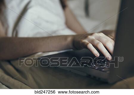 Stock Photograph - Hands of Caucasian woman typing on laptop in bed. Fotosearch