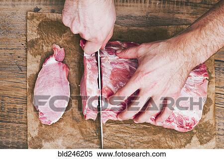 Stock Photography - Hands of man cutting raw meat on butcher paper with knife. Fotosearch