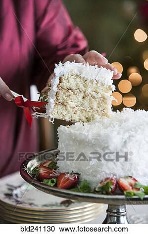 Stock Image - Hands serving slice of coconut cake. Fotosearch
