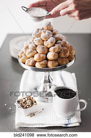 Stock Photo - Hands shaking powdered sugar onto tray of cream puffs. Fotosearch