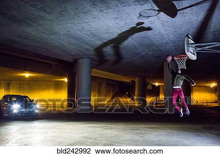Stock Image - Headlights shining on Black man dunking basketball. Fotosearch