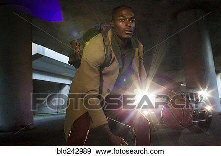 Stock Photo - Headlights shining on Black man wearing backpack playing basketball. Fotosearch