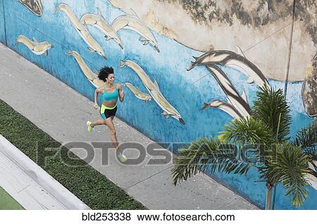 Stock Photo - High angle view of Mixed Race woman running on sidewalk near mural. Fotosearch