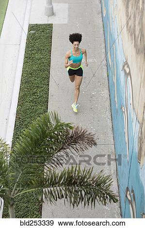 Stock Photo - High angle view of Mixed Race woman running on sidewalk near mural. Fotosearch