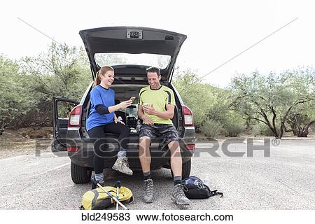 Stock Image - Hikers sitting in car texting on cell phones. Fotosearch