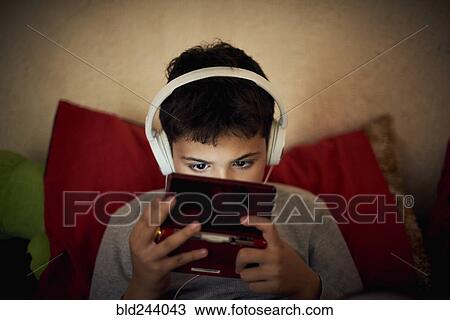 Stock Image - Hispanic boy listening to cell phone with headphones. Fotosearch