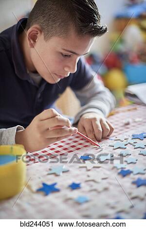 Stock Image - Hispanic boy painting stars at table. Fotosearch