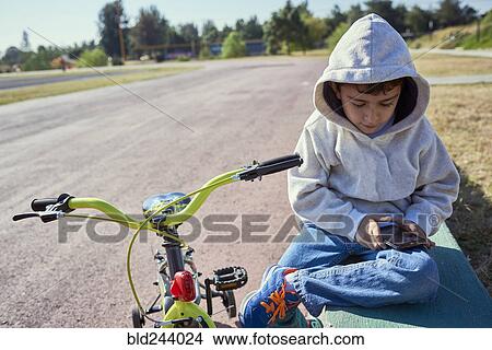 Hispanic boy sitting near bicycle texting on cell phone View Large Photo Image Picture - Hispanic boy sitting near bicycle texting on cell phone. Fotosearch