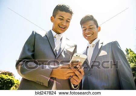 Picture - Hispanic boys wearing suits texting on cell phone. Fotosearch
