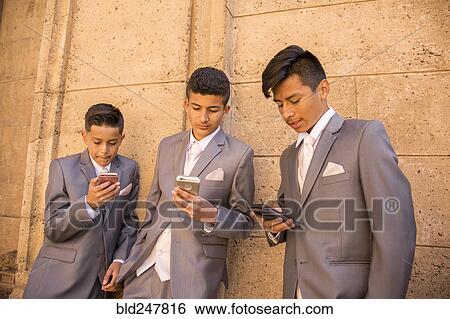 Stock Photograph - Hispanic boys wearing suits texting on cell phones. Fotosearch