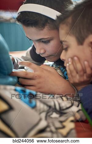Stock Photograph - Hispanic brothers texting on cell phone. Fotosearch