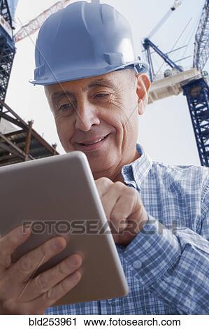 Stock Image - Hispanic construction worker using digital tablet. Fotosearch