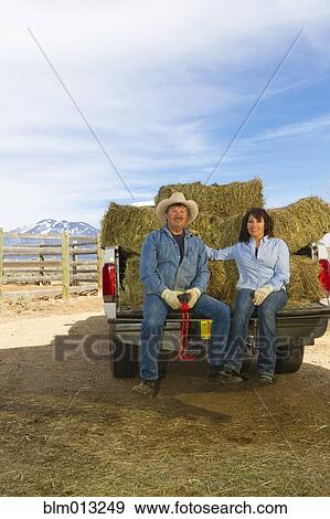 Stock Photo - Hispanic couple sitting on back of truck full of hay. Fotosearch