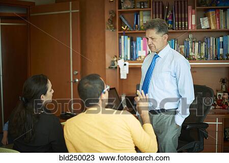 Stock Image - Hispanic couple talking to doctor in office. Fotosearch