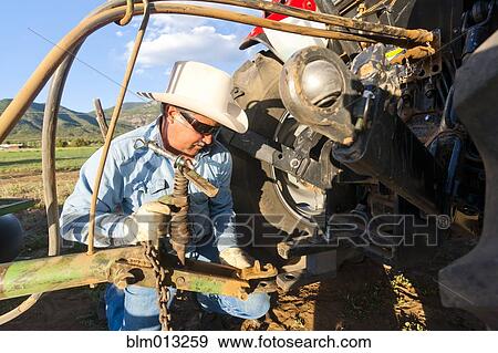 Stock Photo - Hispanic farmer working on tractor. Fotosearch