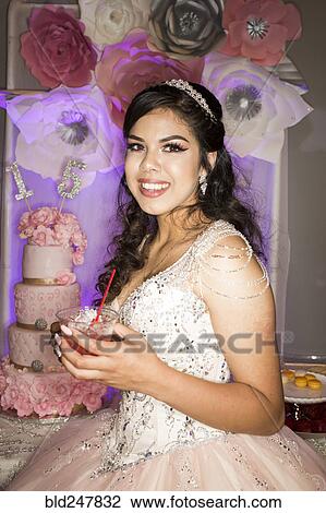 Stock Image - Hispanic girl wearing gown drinking beverage with straw. Fotosearch