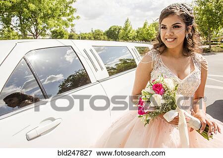 Stock Photo - Hispanic girl wearing gown holding flowers near limousine. Fotosearch