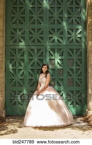 Stock Photo - Hispanic girl wearing gown standing near green wall. Fotosearch