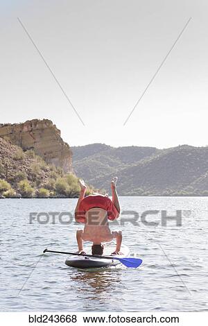 Stock Photo - Hispanic man doing headstand on paddleboard in river. Fotosearch