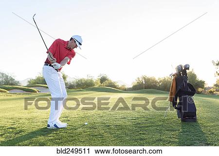Stock Image - Hispanic man hitting ball on golf course. Fotosearch