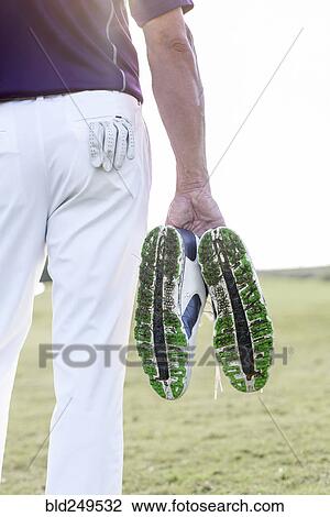 Stock Image - Hispanic man hold golf shoes covered with grass. Fotosearch