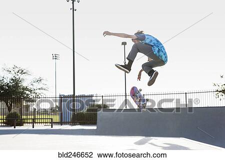 Stock Image - Hispanic man performing mid-air trick on skateboard. Fotosearch