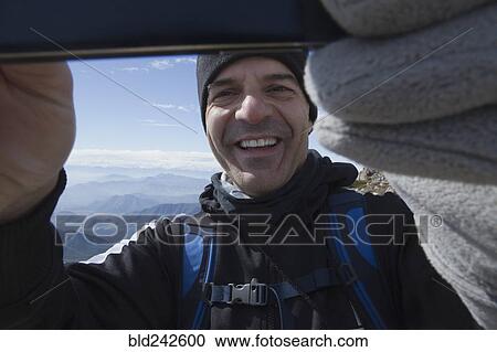Stock Image - Hispanic man posing for cell phone selfie on mountain. Fotosearch