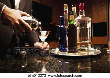 Stock Image - Hispanic man pouring martini in kitchen. Fotosearch