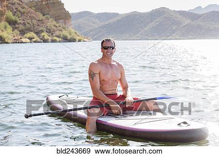 Stock Photo - Hispanic man sitting on paddleboard in river. Fotosearch