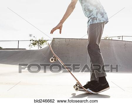 Stock Image - Hispanic man stepping on tail of skateboard. Fotosearch