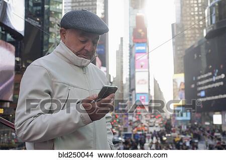 Picture - Hispanic man texting on cell phone in crowded city. Fotosearch