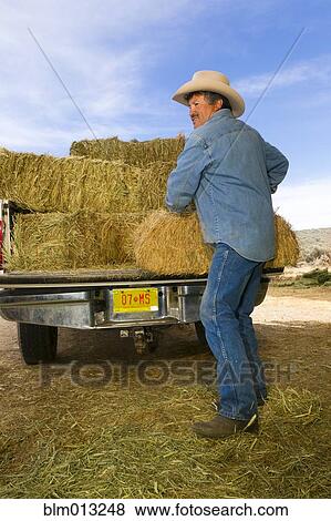 Stock Photo - Hispanic man unloading hay from truck. Fotosearch
