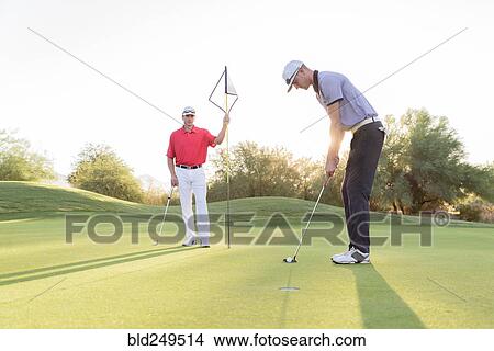 Picture - Hispanic man watching friend on golf course. Fotosearch
