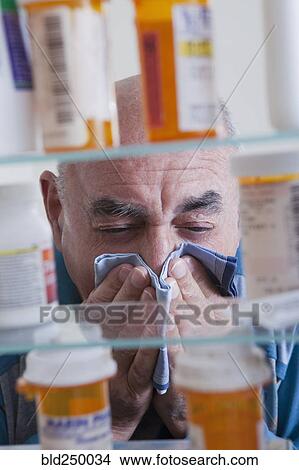 Hispanic man wiping nose near medicine cabinet View Large Photo Image Picture - Hispanic man wiping nose near medicine cabinet. Fotosearch