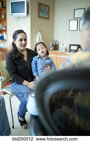 Stock Image - Hispanic mother and daughter with Down Syndrome talking to doctor. Fotosearch