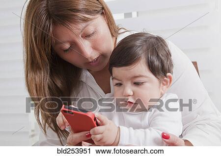 Hispanic mother holding baby boy playing with cell phone View Large Photo Image Stock Image - Hispanic mother holding baby boy playing with cell phone. Fotosearch