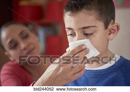 Stock Image - Hispanic mother wiping nose of son with tissue. Fotosearch