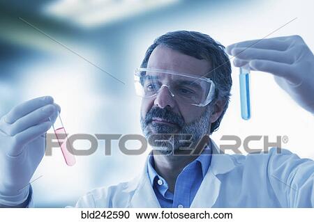 Stock Image - Hispanic researcher holding vials of red and blue liquid. Fotosearch