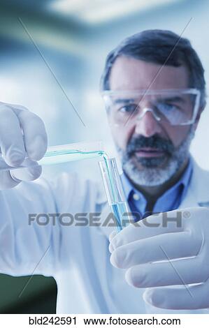Stock Image - Hispanic researcher mixing vials of liquid. Fotosearch