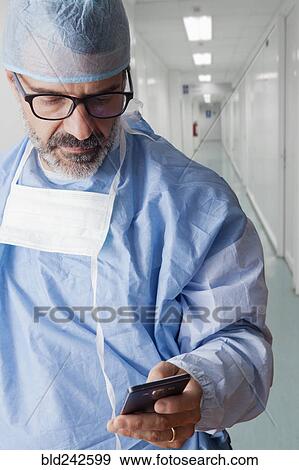 Stock Photo - Hispanic surgeon texting on cell phone. Fotosearch
