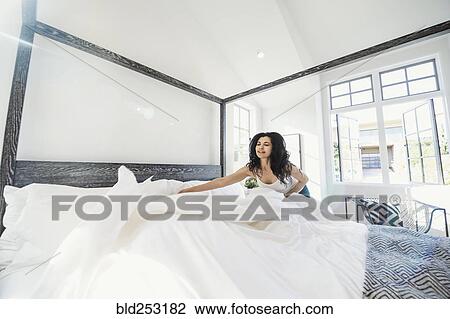 Stock Image - Hispanic woman arranging comforter on bed. Fotosearch