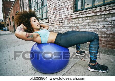 Picture - Hispanic woman balancing on fitness ball near brick wall. Fotosearch