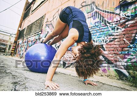 Stock Photo - Hispanic woman balancing on fitness ball near graffiti wall. Fotosearch