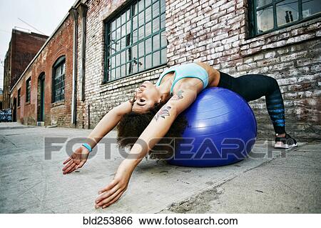Stock Photograph - Hispanic woman balancing on fitness ball near brick wall. Fotosearch